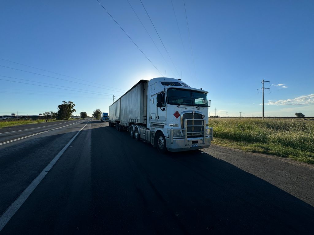A silver semi truck driving on an open highway under a clear blue sky.